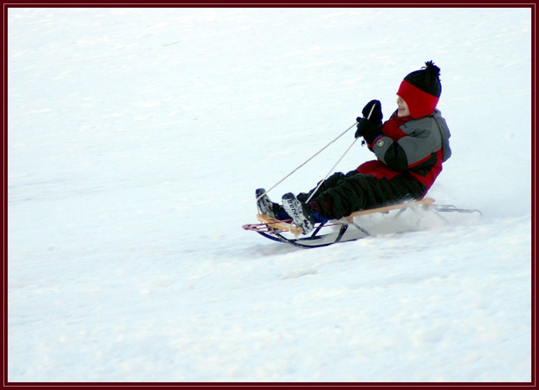 A young child sledding down a large hill after a snowstorm. He was obviously having a lot of fun. This just before sunset and the sun was low behind some trees.